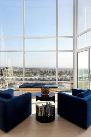 Ein modernes Wohnzimmer mit großem Fenster, zwei blauen Sofas, einem kleinen Couchtisch und einem Bücherregal.