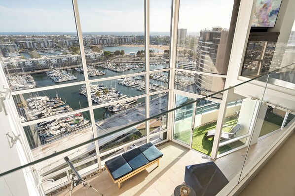 Ein Hotelzimmer in einem Hochhaus mit großen Fenstern und Blick auf einen Yachthafen und die Stadtlandschaft.