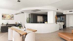 Et moderne køkken med en central ø, et spiseområde med et træbord og et opholdsområde med en lædersofa.