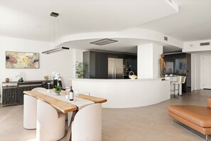 Eine moderne Küche mit einer zentralen Kochinsel, einem Essbereich mit Holztisch und einer Sitzecke mit Ledersofa.