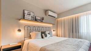 Une chambre moderne avec un lit, des tables de chevet, un climatiseur fixé au mur et une fenêtre avec des rideaux.