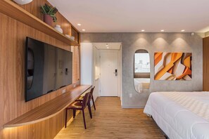 Une chambre d’hôtel moderne avec un bureau en bois, une grande télévision à écran plat, un lit et une vue sur la ville.