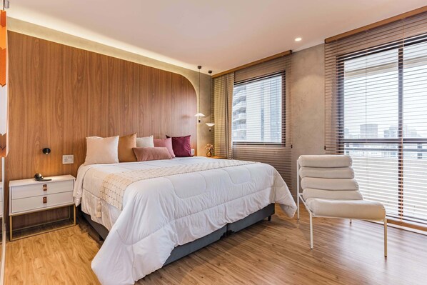 A modern bedroom with a large bed, bedside tables, a chair, and large windows with blinds. - #QL1606 | Cyclinn Faria Lima Pinheiros (Pinheiros)