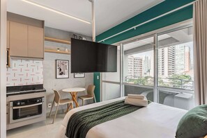 Ein Hotelzimmer mit Bett, einer Küchenzeile, einem Essbereich und einem großen Fenster mit Blick auf die Stadt.