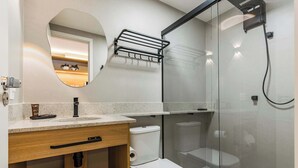 Ein modernes Badezimmer mit einer Duschkabine aus Glas, einer weißen Toilette, einem Waschbecken mit Handtuchhalter und einem Spiegel.
