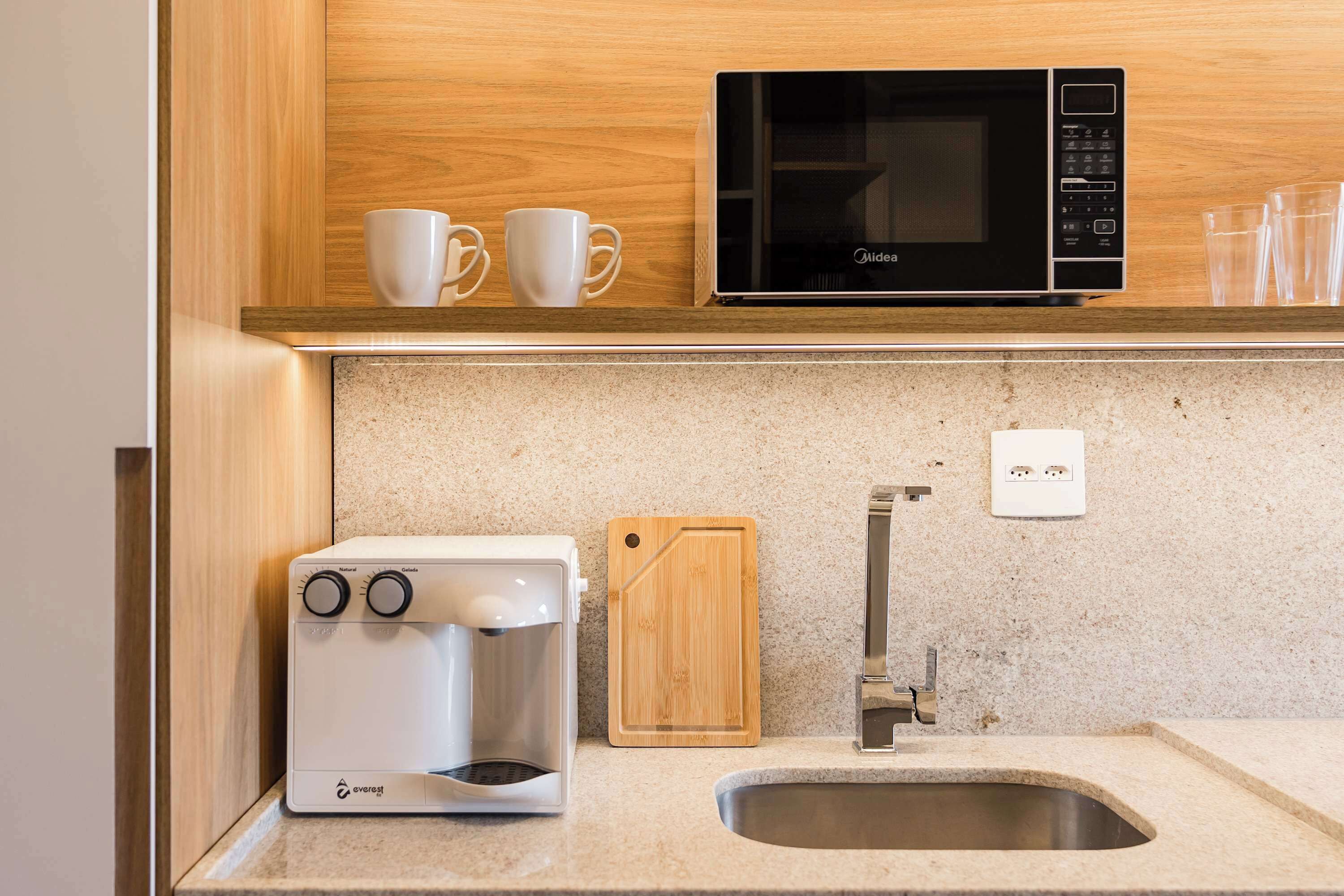 A kitchen with a coffee maker, a microwave, a cutting board, and a sink.