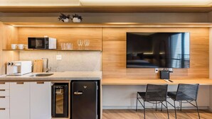Eine moderne Küche mit integriertem Mikrowellenherd, Toaster und Kühlschrank, ein Essbereich mit zwei Stühlen sowie ein großer Flachbildfernseher an der Wand.