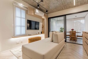 A modern living room with a sofa, a flat-screen TV, a dining area with a table and chairs, and a sliding glass door leading to a balcony. - #AT32 | Cyclinn Itaim Jesuino (Itaim Bibi)