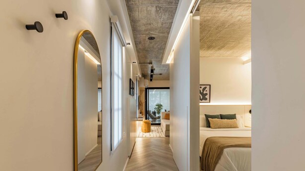 Um corredor com um espelho grande, uma cama com cabeceira e uma mesa de cabeceira.