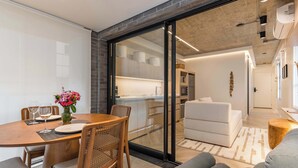 Um interior moderno com área de jantar, sofá e cozinha visível através de uma porta de vidro.