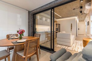 A modern interior with a dining area, a sofa, and a kitchen visible through a glass door. - #AT32 | Cyclinn Itaim Jesuino (Itaim Bibi)