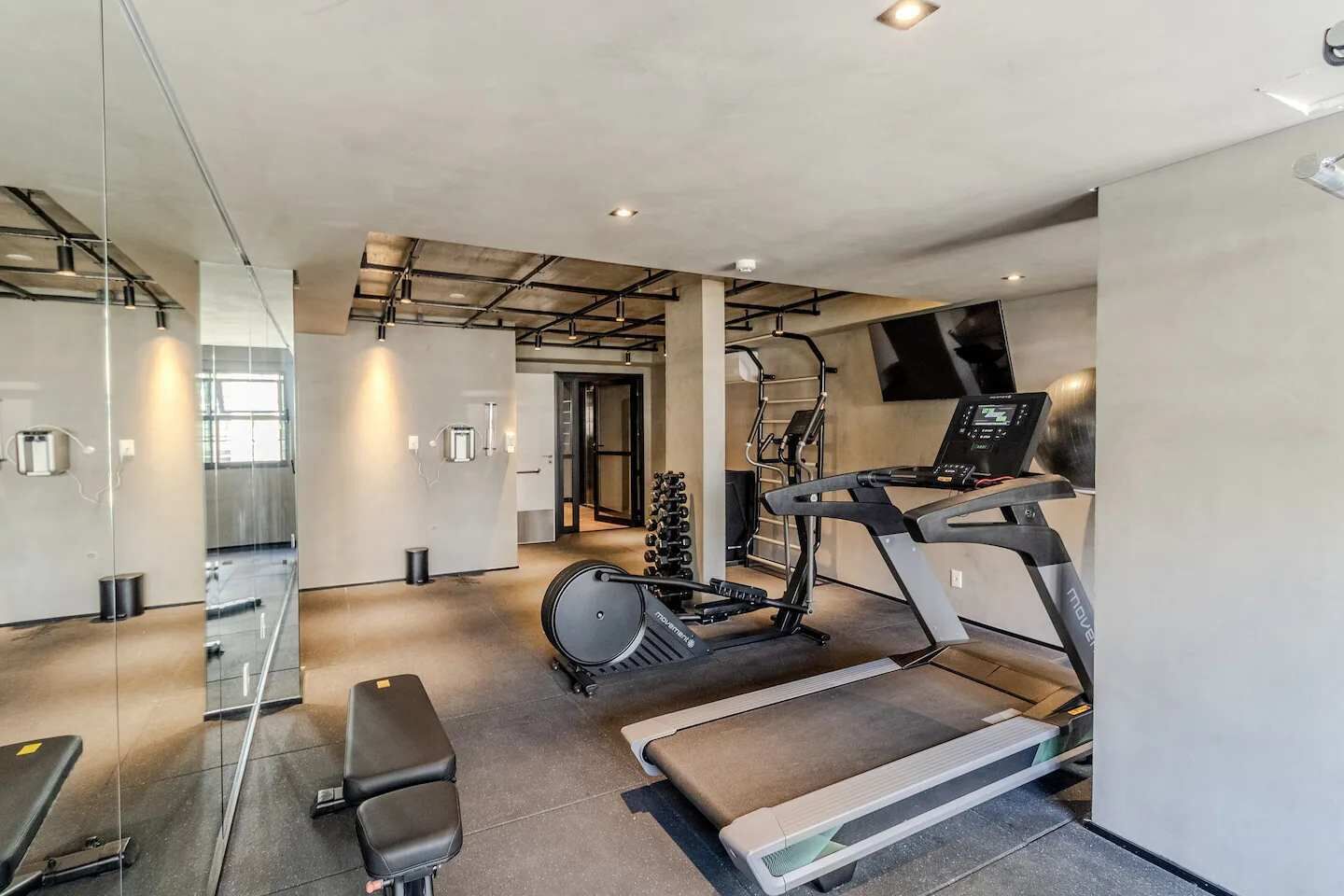Ein modernes Fitnessstudio mit Laufband, Ergometer und einer Gewichtshalterung.