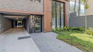 Um edifício moderno com entrada coberta, porta de vidro e um pequeno jardim.