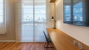 Une chambre moderne avec un bureau en bois, un lampadaire, un vélo et une grande fenêtre donnant sur la ville.