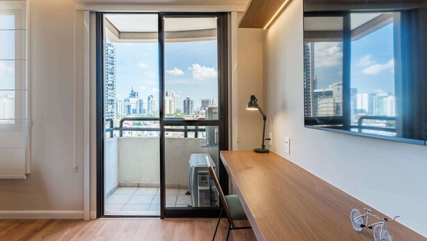 Une chambre moderne avec un bureau en bois, un vélo et une vue sur la ville, visible à travers une porte coulissante.