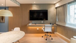 Un espacio de oficina moderno con un televisor de pantalla plana grande montado en la pared, un panel de pared de madera, una silla de oficina blanca y una mesa de mármol.