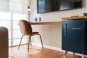 Ein modernes Zimmer mit Holzboden, einem braunen Stuhl, einem dunkelblauen Schrank mit Griff und einem angebrachten Fernseher. Eine kleine Fahrrad-Dekoration ist ebenfalls vorhanden.