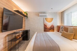A modern bedroom with a large bed, a flat-screen TV, a built-in air conditioner, and a brick wall. - #WP302 | Cyclinn Paulista Jardins (Jardim Paulista)