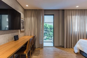 Ein modernes Hotelzimmer mit Schreibtisch aus Holz, einem Bett und einem Balkon mit Vorhängen.