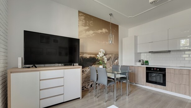 A modern kitchen with a flat-screen TV, dining table with chairs, and a built-in oven. - Nadmorski Zakątek by Grand Apartments (Sopot)