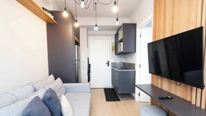 Ett modernt vardagsrum med en soffa, en platt-TV som är monterad på en vägg av trä, och ett köksområde i bakgrunden.