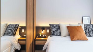 Ett hotellrum med en vägg som är täckt av speglar, två sängar med mönstrade kuddar, ett sängbord med en lampa och en liten växt.