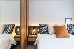 A hotel room with a mirrored wall, two beds with patterned pillows, a bedside table with a lamp, and a small plant. - Studio Completo na Av. Santo Amaro | NI1802 (Vila Nova Conceição)