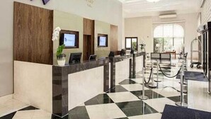 Zona de recepción de un hotel con un mostrador de registro, dos monitores y un amplio ventanal que proporciona luz natural.