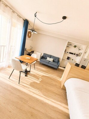 A modern, well-lit room with a wooden dining table, a sofa, a bed, and a bookshelf. - Le BlueAna – Studio moderne & confortable (Poitiers)