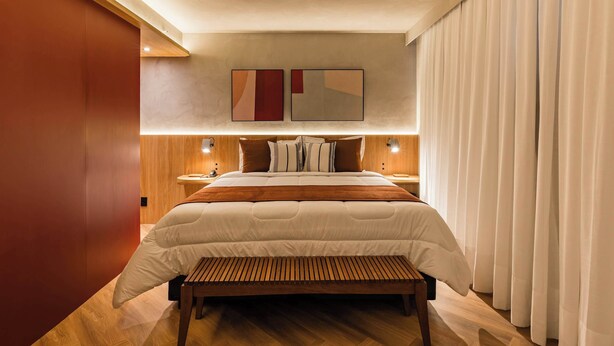 Une chambre à coucher moderne avec un grand lit, une tête de lit en bois, des tables de chevet et un banc.