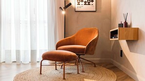 Une pièce moderne avec un tapis rond en fibres tressées, un fauteuil marron recouvert de tissu, une petite étagère en bois et un tableau encadré accroché au mur.
