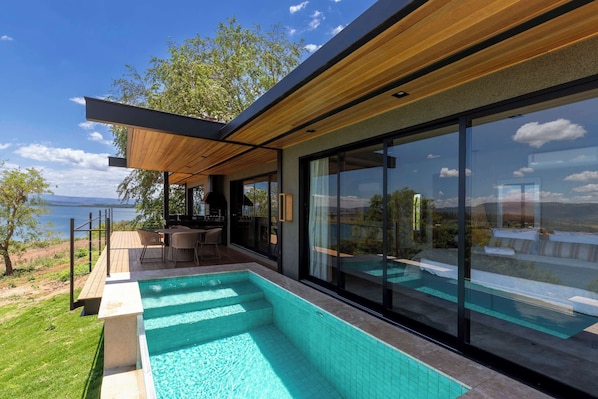 A modern outdoor pool area with a view of the sea, wooden deck, and glass-enclosed seating.