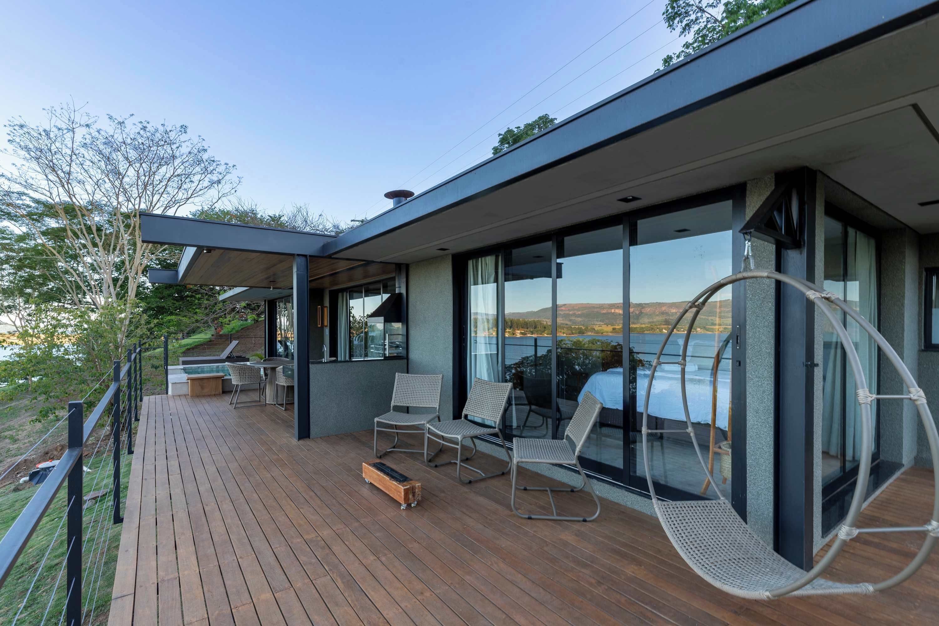A modern outdoor deck with wooden flooring, seating, and a glass balustrade overlooking a scenic landscape.
