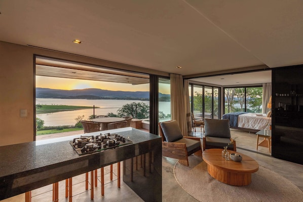 Un interior moderno con barra en la cocina, zona de estar y un dormitorio con ventana grande con vistas al agua.