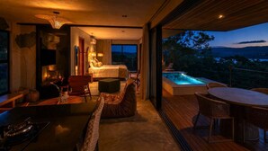 Un dormitorio moderno con una cama grande, un rincón de estar con una mesa y sillas, y vistas a un jacuzzi y el paisaje.