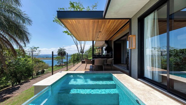 Un área de piscina moderna al aire libre con escalones que bajan al agua, una terraza de madera y vistas al océano.