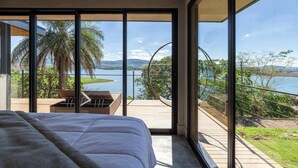 Een slaapkamer met een groot bed, uitzicht op een meer en een balkon met een hangmat.