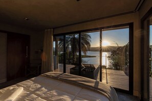 A bedroom with a large bed, a view of a lake, and a balcony with outdoor furniture.