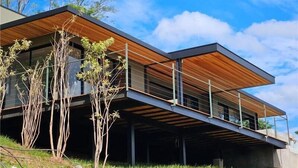 Una casa moderna de dos pisos con techo plano, ventanas grandes y una terraza de madera.