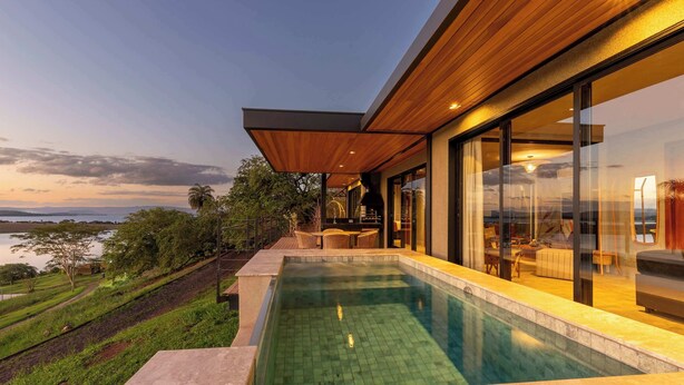 Ein moderner Poolbereich mit Blick aufs Wasser, Gartenmöbel und eine überdachte Sitzgruppe.