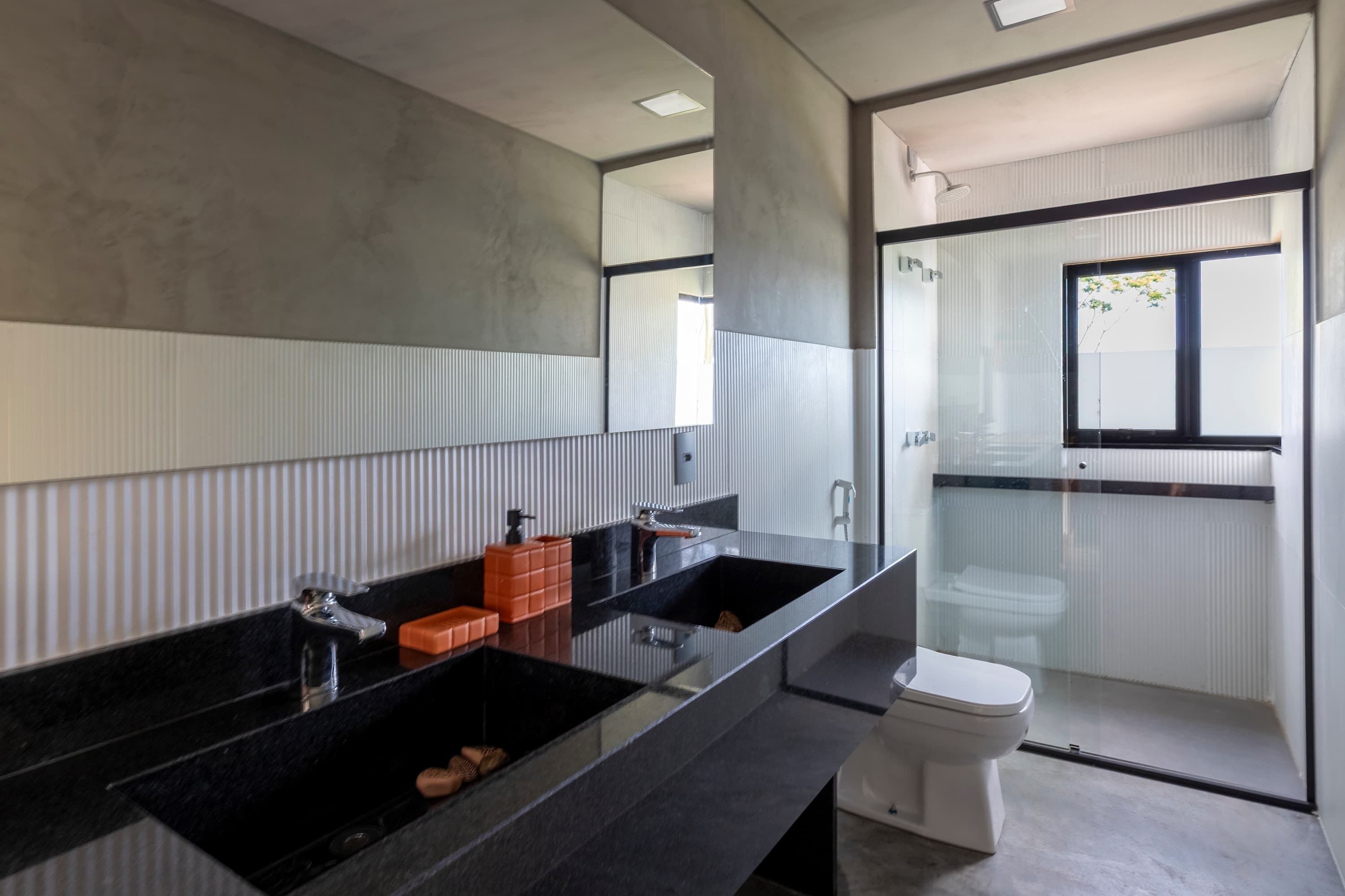 A modern bathroom with a large mirror, two black sinks, a toilet, and a glass shower enclosure.