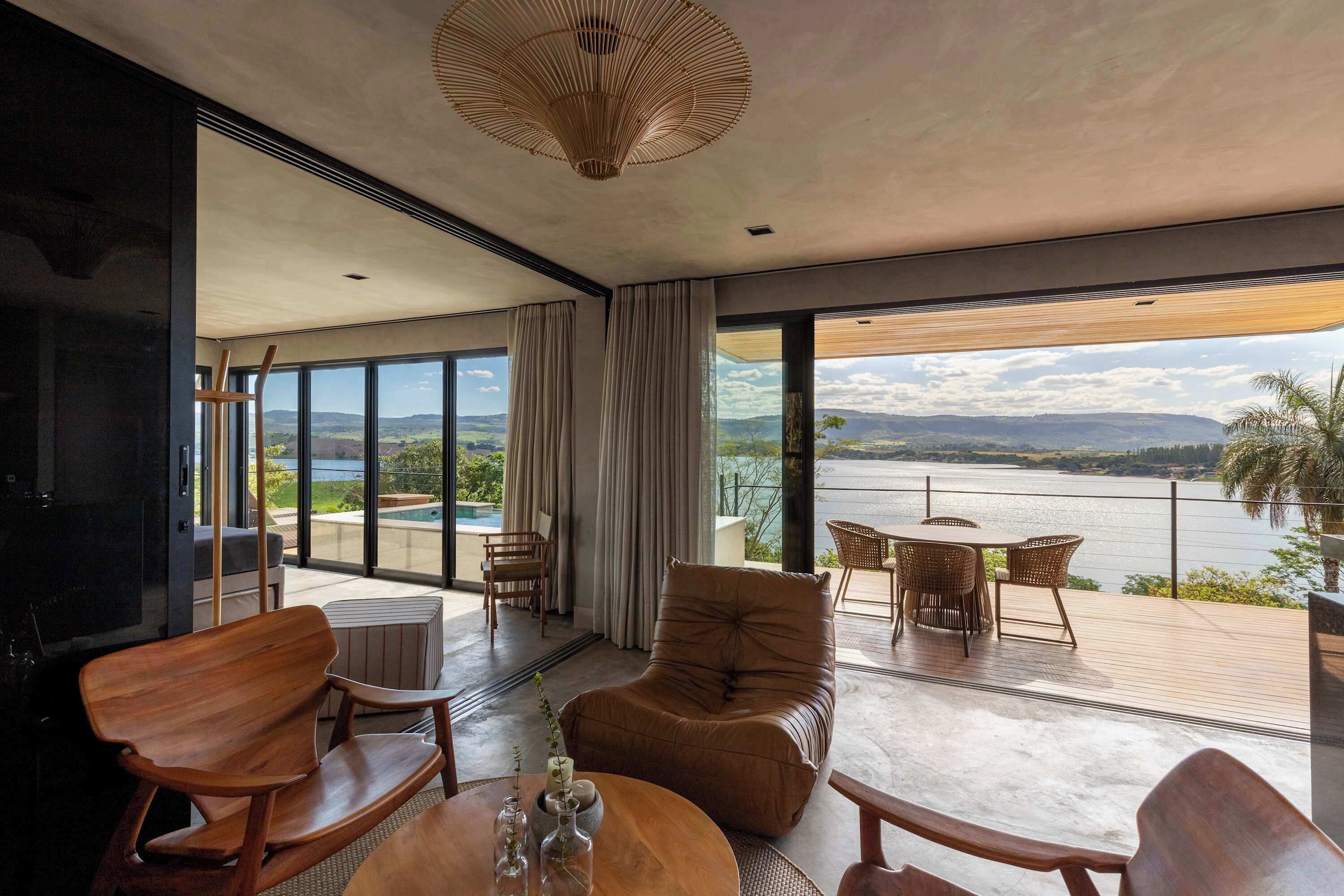 A modern interior with a large window overlooking a body of water, a wooden deck, and a seating area with a table and chairs.