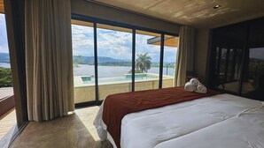 Ein Hotelzimmer mit einem großen Bett, Blick auf einen Swimmingpool und einem Balkon mit Wasserblick.