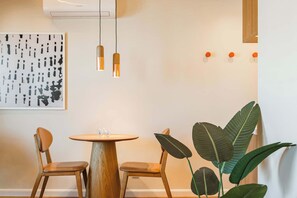 A dining area with a round wooden table, two chairs, pendant lights, a wall-mounted air conditioner, a large abstract painting, and a potted plant. - #TP1203 | Cyclinn Perdizes (Perdizes)