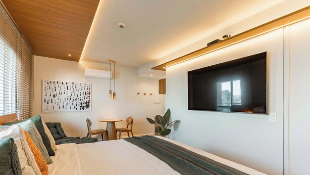 Een moderne hotelkamer met een groot bed, een aan de muur bevestigde televisie, een zithoek en een plant.