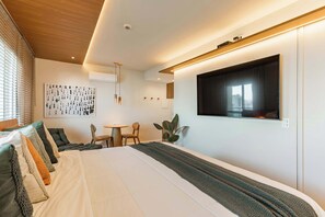 Una habitación de hotel moderna con una cama grande, un televisor montado en la pared, una zona de comedor y una planta.