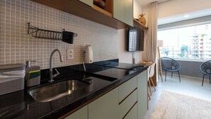 Eine moderne Küche mit schwarzem Arbeitsplatz, Spüle aus Edelstahl und einer gefliesten Spritzschutzwand. Es gibt einen Essbereich mit einem Stuhl und einem an der Wand montierten Fernseher.