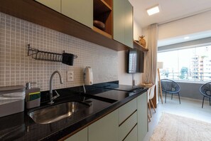 Eine moderne Küche mit schwarzem Arbeitsplatz, Spüle aus Edelstahl und einer gefliesten Spritzschutzwand. Es gibt einen Essbereich mit einem Stuhl und einem an der Wand montierten Fernseher.