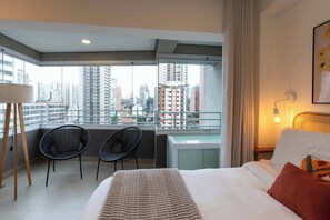 Ein Hotelzimmer mit Bett, zwei Stühlen, einem Balkon mit Stadtblick und einer Wandlampe.
