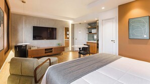 Une chambre d’hôtel moderne dotée d’un grand lit, d’une télévision, d’un coin salon avec une table et des chaises, et d’une kitchenette.